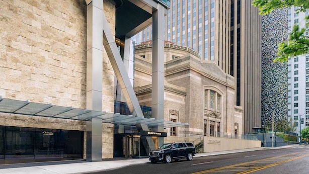 Un hôtel moderne à la façade classique, doté d’une entrée en verre et devant lequel est garé un SUV noir.