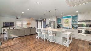 Een moderne keuken met witte kastjes, een centraal eiland met barstoelen, en een groot eiland met een ingebouwde oven.
