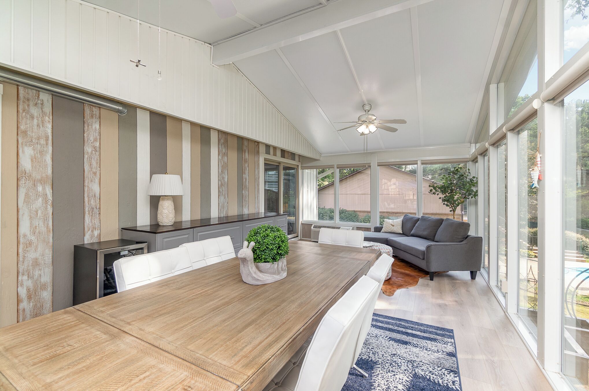 Un espace repas moderne avec une table en bois, des chaises blanches et un canapé gris.