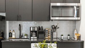 Una cocina moderna con gabinetes grises, un microondas de acero inoxidable, una cafetera y diversos utensilios de cocina.