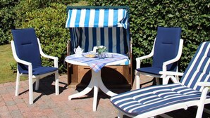 Eine Terrasse mit zwei Liegestühlen, einem kleinen Tisch und einem gestreiften Sonnenschirm.