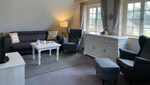 Ein Wohnzimmer mit einem dunklen Sofa, einem weißen Couchtisch, einem grauen Sessel und einer weißen Kommode.