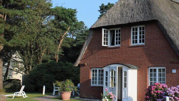 Ein traditionelles Haus mit Strohdach, einer Ziegelaußenwand, einer weißen Tür und Fenstern mit weißen Rahmen.