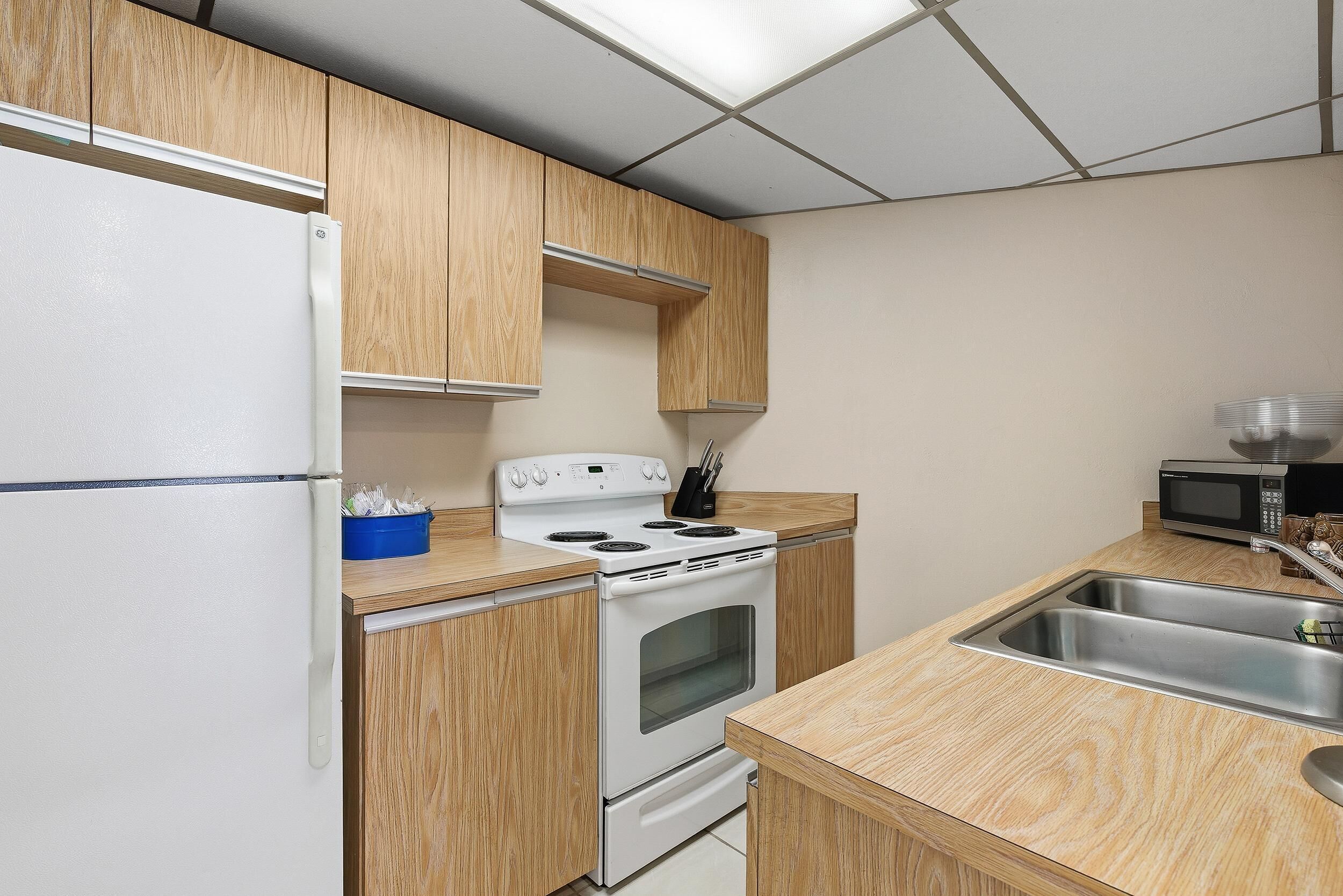 A compact kitchen with wooden cabinets, a white refrigerator, a stove, and a microwave.