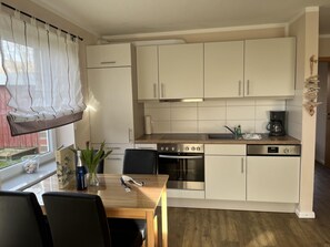 A compact kitchen with a dining area, featuring a stove, oven, and coffee maker. - Fiete's Small Vacation Apartment (Wittdün)