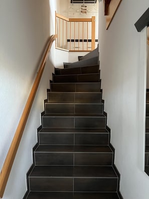 A staircase with dark tiles and a wooden handrail, leading to a landing with a wooden railing. - Spacious Fiete Vacation Apartment (Wittdün)