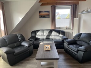 A living room with a black leather sofa set, a wooden coffee table, and a window with curtains. - Large Fiete vacation apartment (Wittdün)