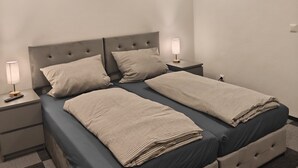 Ein Doppelbett mit einem geblatteten Kopfteil, zwei Nachttische mit Lampen und ein Schachbrettmuster Boden.