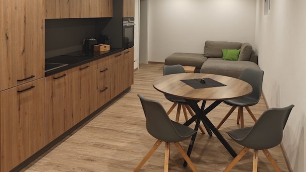 Eine moderne Küche mit Holzausstattung, ein Essbereich mit rundem Tisch und Stühlen sowie eine Couch im Hintergrund.