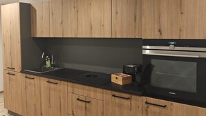 Eine moderne Küche mit Holzausstattung, einer schwarzen Arbeitsplatte, einem Siemens-Ofen und einer Kaffeemaschine.