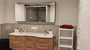 Ein modernes Badezimmer mit zwei Waschbecken, einem großen Spiegel und einer Duschkabine aus Glas.