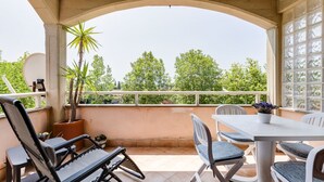Un espacio de estar techado al aire libre con una mesa, sillas, una planta en maceta y vistas a árboles.