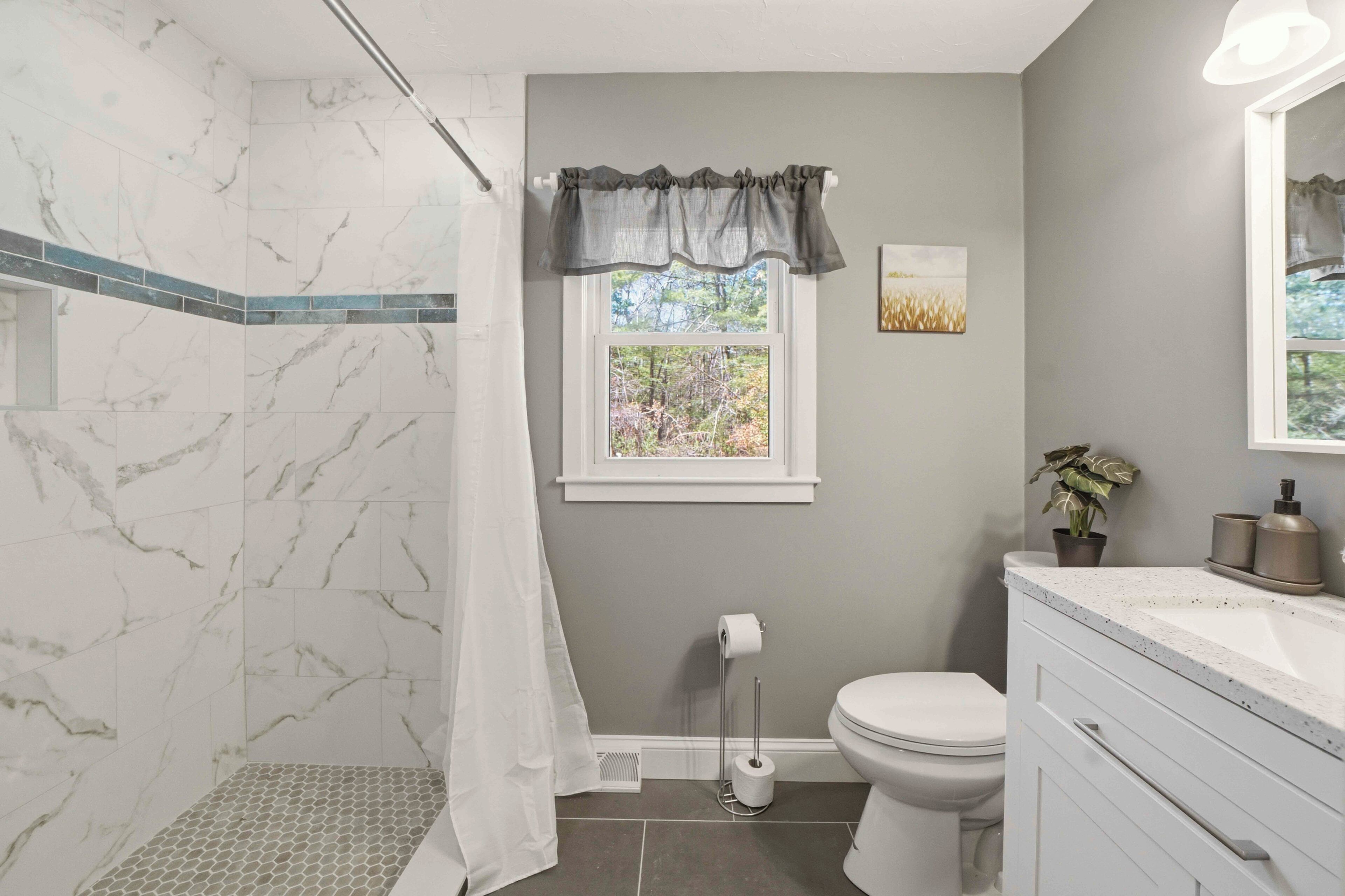 Baño con ducha, inodoro, lavamanos y ventana.
