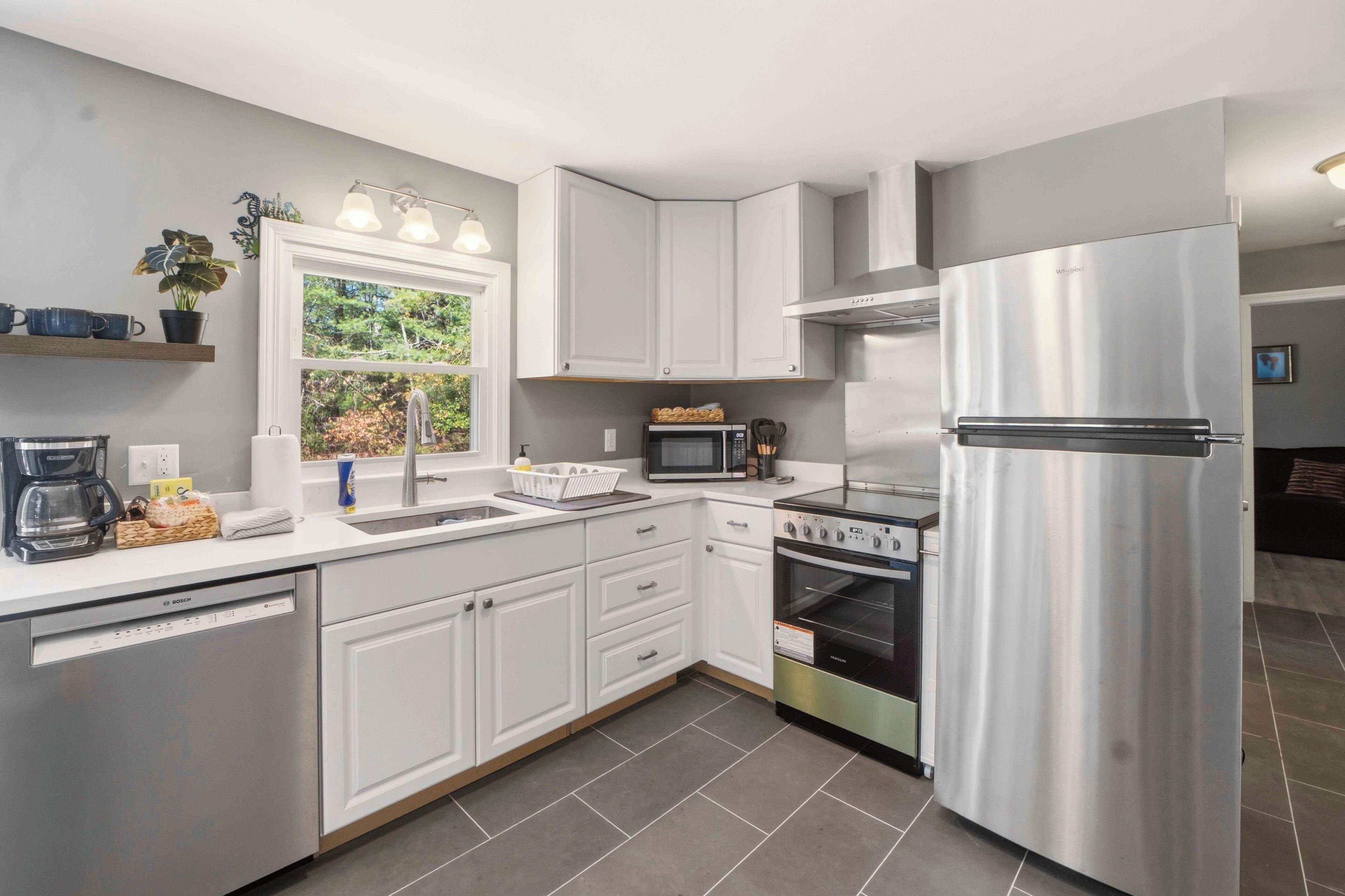 A modern kitchen with white cabinetry, a stainless steel refrigerator, a built-in oven, a microwave, and a dishwasher.