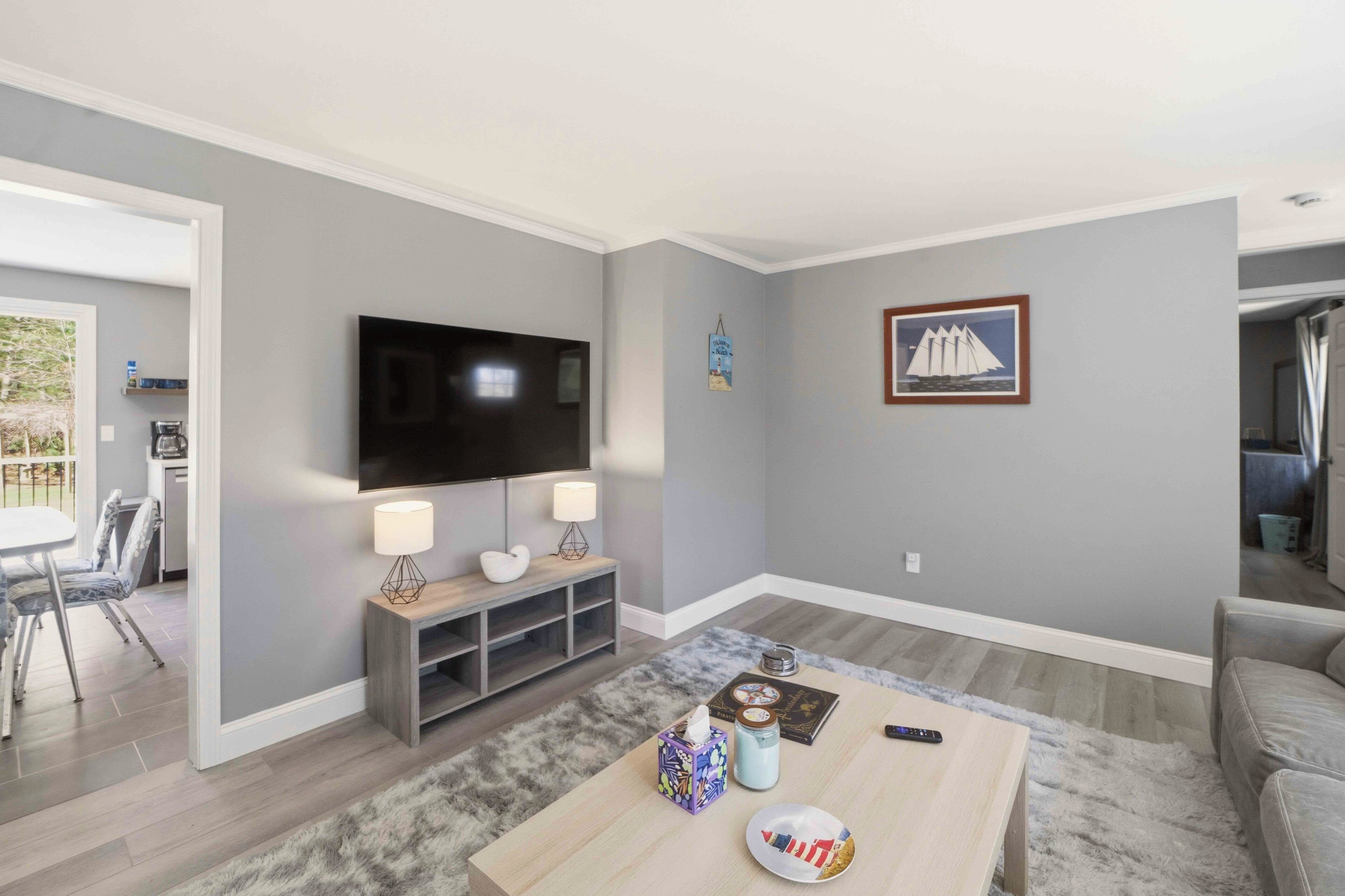 Una sala de estar moderna con un televisor de pantalla plana, dos lámparas, una mesa de centro con control remoto y un cuadro enmarcado en la pared.
