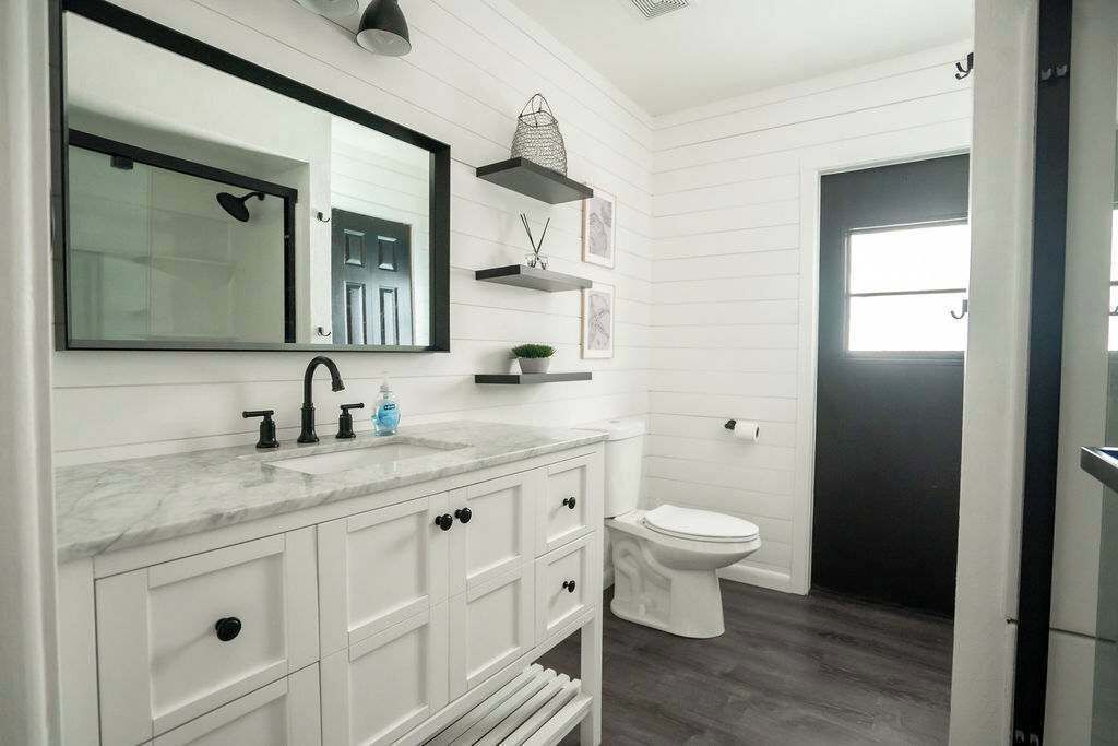 Een badkamer met een wit wastafelmeubel, een grote spiegel, een moderne wastafel, een toilet en een donkere deur.