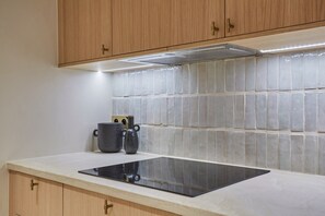 Een keuken met houten kastjes, een betegelde achterwand en een zwart inductiekooktoestel.