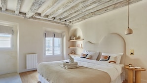 A bedroom with a large bed, wooden beams on the ceiling, a bedside table, and a window with curtains. - Luxurious Apartment Place Vendome - Rue de la Paix (Paris)