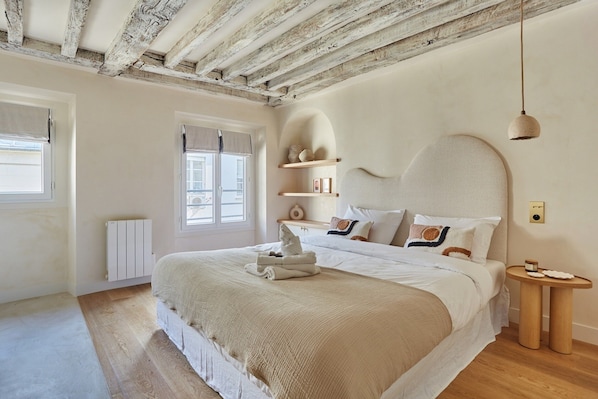 Une chambre avec un grand lit, des poutres en bois au plafond, une table de chevet et une fenêtre avec des rideaux.