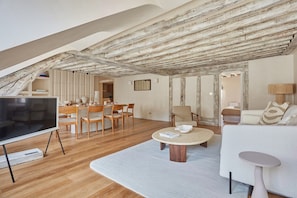 A spacious living area with a wooden ceiling, a dining table with chairs, a sofa, a coffee table, and a TV. - Luxurious Apartment Place Vendome - Rue de la Paix (Paris)