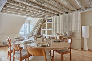 A dining area with a round table set for six, wooden chairs, and a high ceiling with exposed beams. - Luxurious Apartment Place Vendome - Rue de la Paix (Paris)