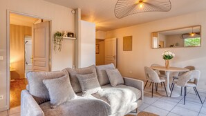 Ett modernt vardagsrum med en grå soffa, ett matbord med stolar, en hängande lampa och en spegel på väggen.