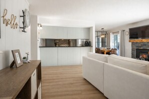 A modern living room with a white sofa, wooden flooring, and a kitchen in the background. - Walk to Ski Beautifully Renovated 2BR 2BA 645 (Mammoth lakes)