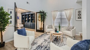 A spacious living room with a large window, a built-in bookshelf, and a dining area visible through an open door. - The Casa Cantera by Six Flags, La Cantera, The Rim. 3Br Home with Pool & Cabana (San Antonio)