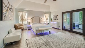 A spacious bedroom with a large bed, a ceiling fan, a sitting area with a chair and ottoman, and a view through a glass door. - The Casa Cantera by Six Flags, La Cantera, The Rim. 3Br Home with Pool & Cabana (San Antonio)