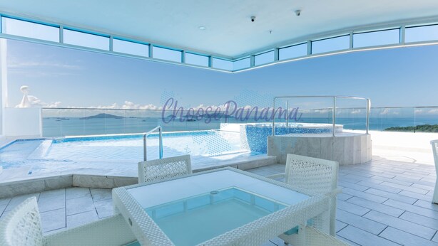 A modern outdoor pool area with a glass table and white wicker chairs, overlooking a scenic ocean view. - 23M Spectacular New Penthouse Oceanview (Panama City)