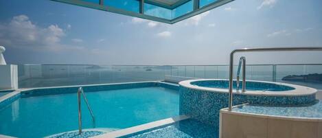 A rooftop infinity pool with clear blue water, surrounded by a glass balustrade, and offering a view of the ocean.