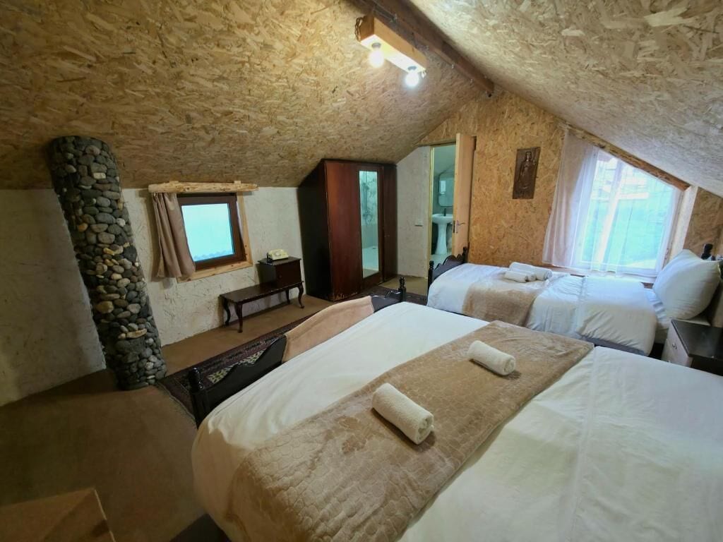 A cozy attic bedroom with two beds, a stone pillar, and a small desk.