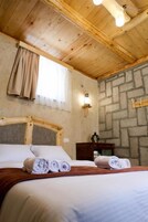 Techo de madera, pared de piedra, cama con sábanas blancas y mesita de noche con lámpara.