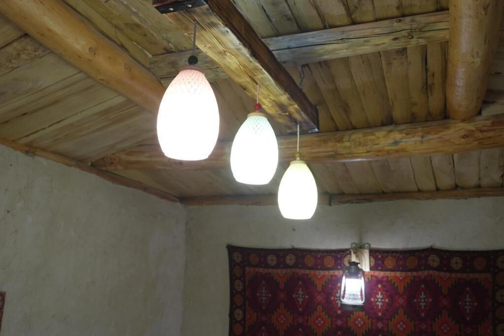A room with wooden beams on the ceiling, a patterned tapestry on the wall, and hanging light fixtures.