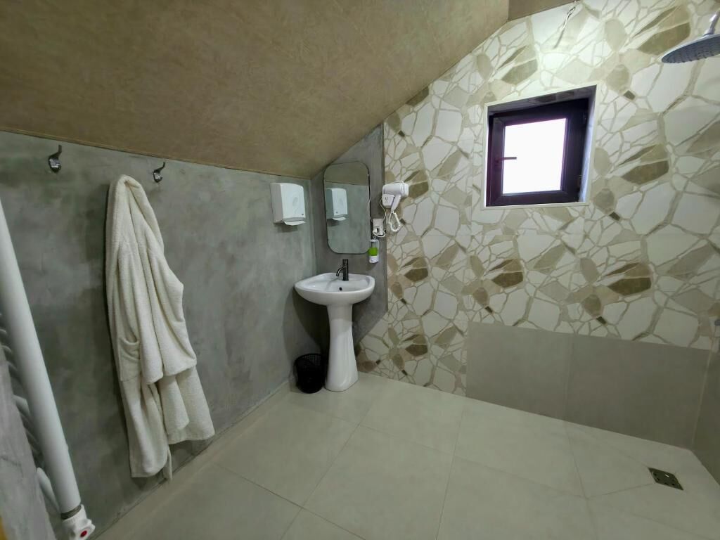 A bathroom with a stone-patterned wall, a sink, a towel rack, and a window.