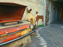 Un coche antiguo con el capó abierto, una pared rústica con un mural de un ciervo y una rueda de bicicleta.