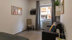 Habitació moderna amb llit, sofà, cadira, televisió i finestra amb cortines.