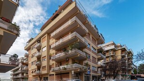 Un edifici d'apartaments de diversos pisos amb balcons, una zona d'aparcament i un cel serè.