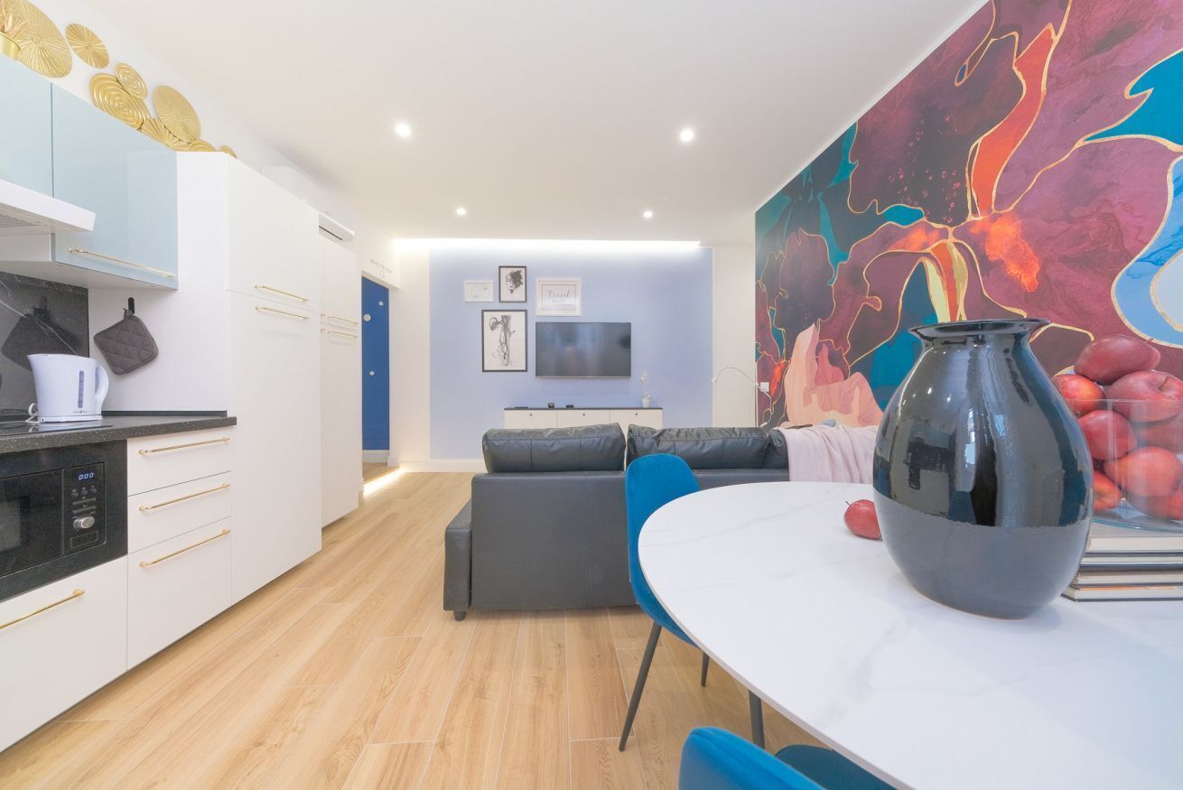 A modern kitchen with white cabinets, a built-in oven, and a dining area with a white table and blue chairs.