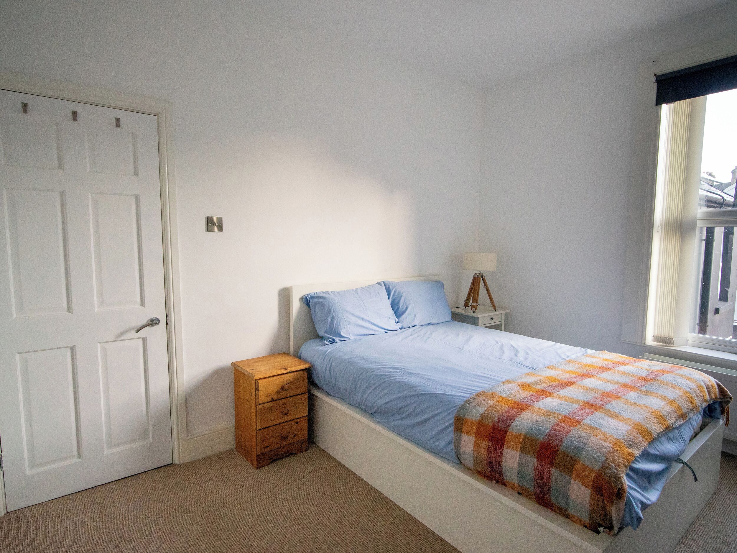 A bedroom with a bed, a wooden nightstand, a lamp, and a window with curtains.