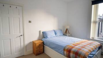A bedroom with a bed, a wooden nightstand, a lamp, and a window with curtains.