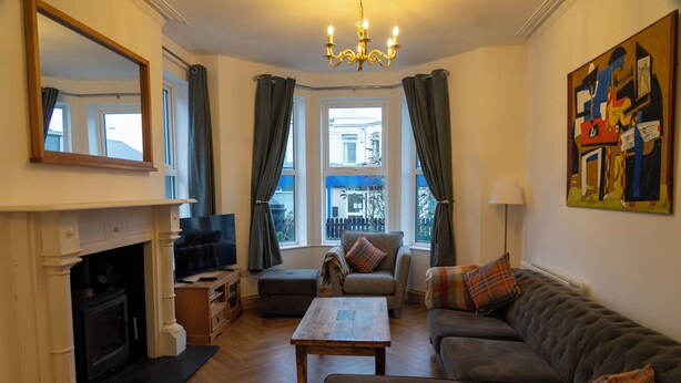 A living room with a fireplace, a sofa, a coffee table, and a painting on the wall. - The Red Door (Bangor)