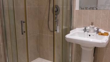 A bathroom with a glass-enclosed shower, a white sink with two faucets, and a soap dispenser.