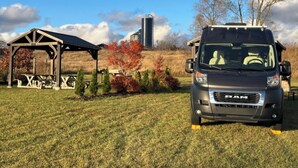 Una camioneta RAM negra estacionada en un área con césped, con un porche de madera y un silo al fondo.