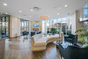 A spacious lobby with a curved sofa, a chandelier, and a TV on the wall. - Skyline Vista | Penthouse | Views | Gym | Theatre (Niagara Falls)