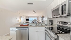A modern kitchen with white cabinets, stainless steel appliances, and a large window providing natural light. - Carlos Pointe #624 (Fort Myers Beach)