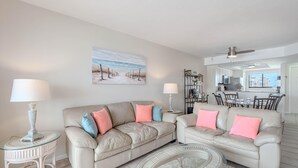 A living room with two beige sofas, a glass coffee table, and a dining area with a white table and chairs. - Carlos Pointe #624 (Fort Myers Beach)