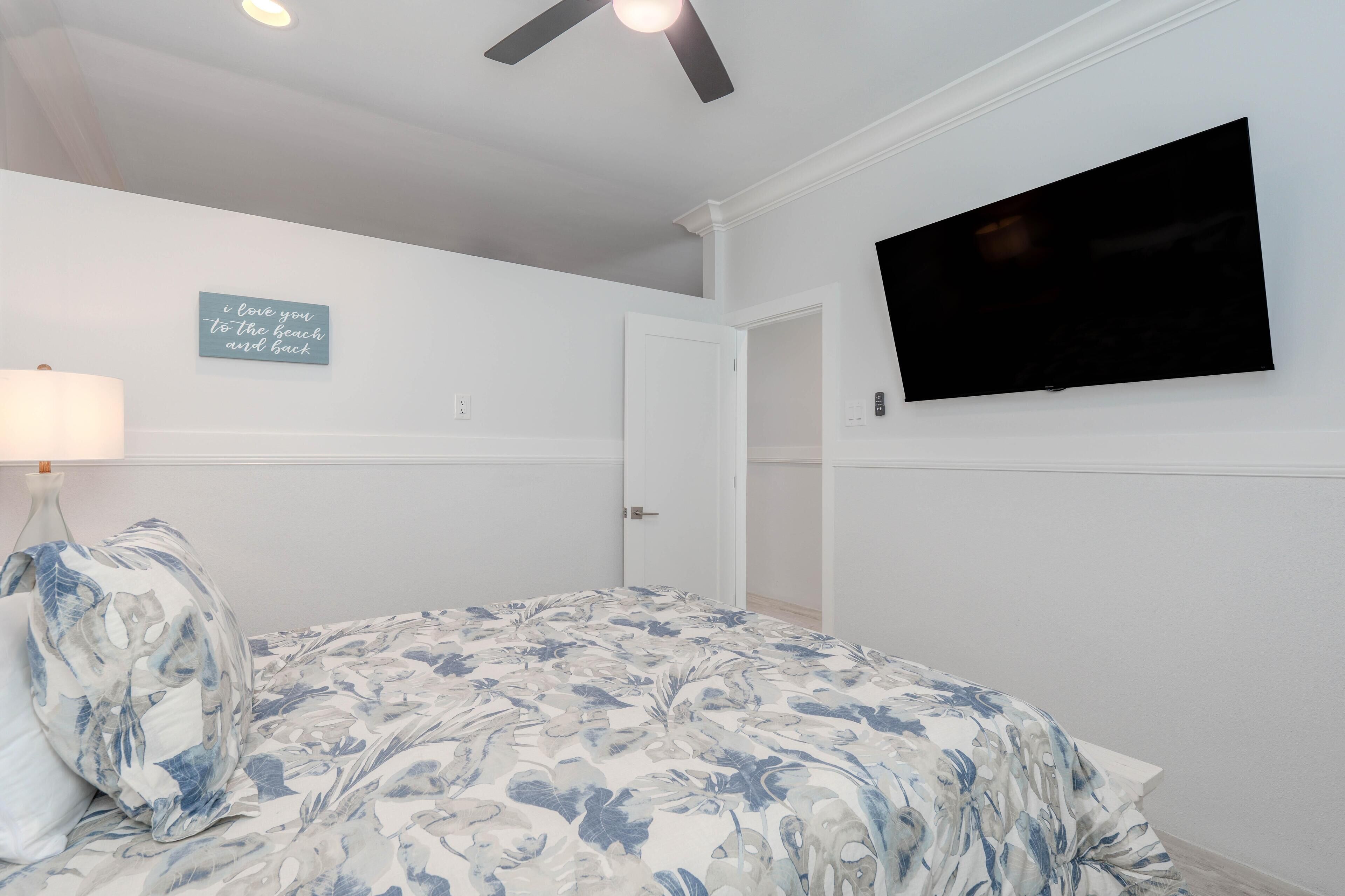 A bedroom with a bed, a television on the wall, a door, and a sign on the wall.