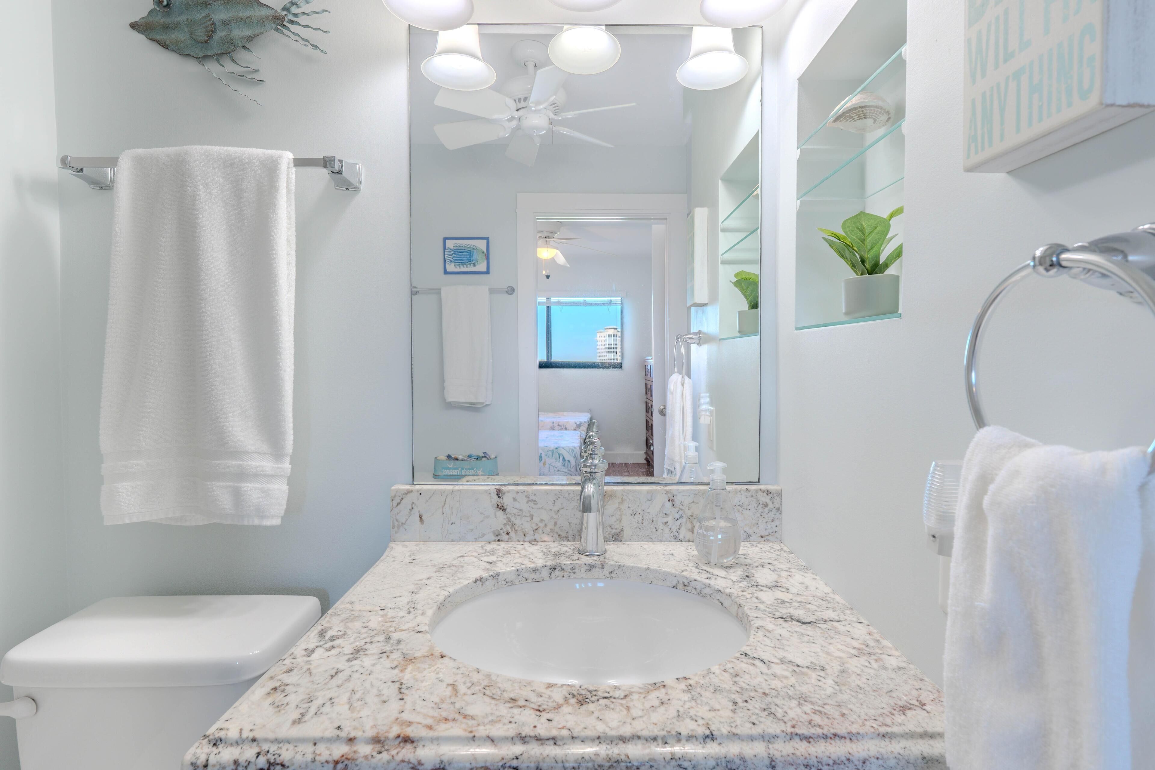 Une salle de bain avec un lavabo blanc, des toilettes, un ventilateur de plafond et un miroir.