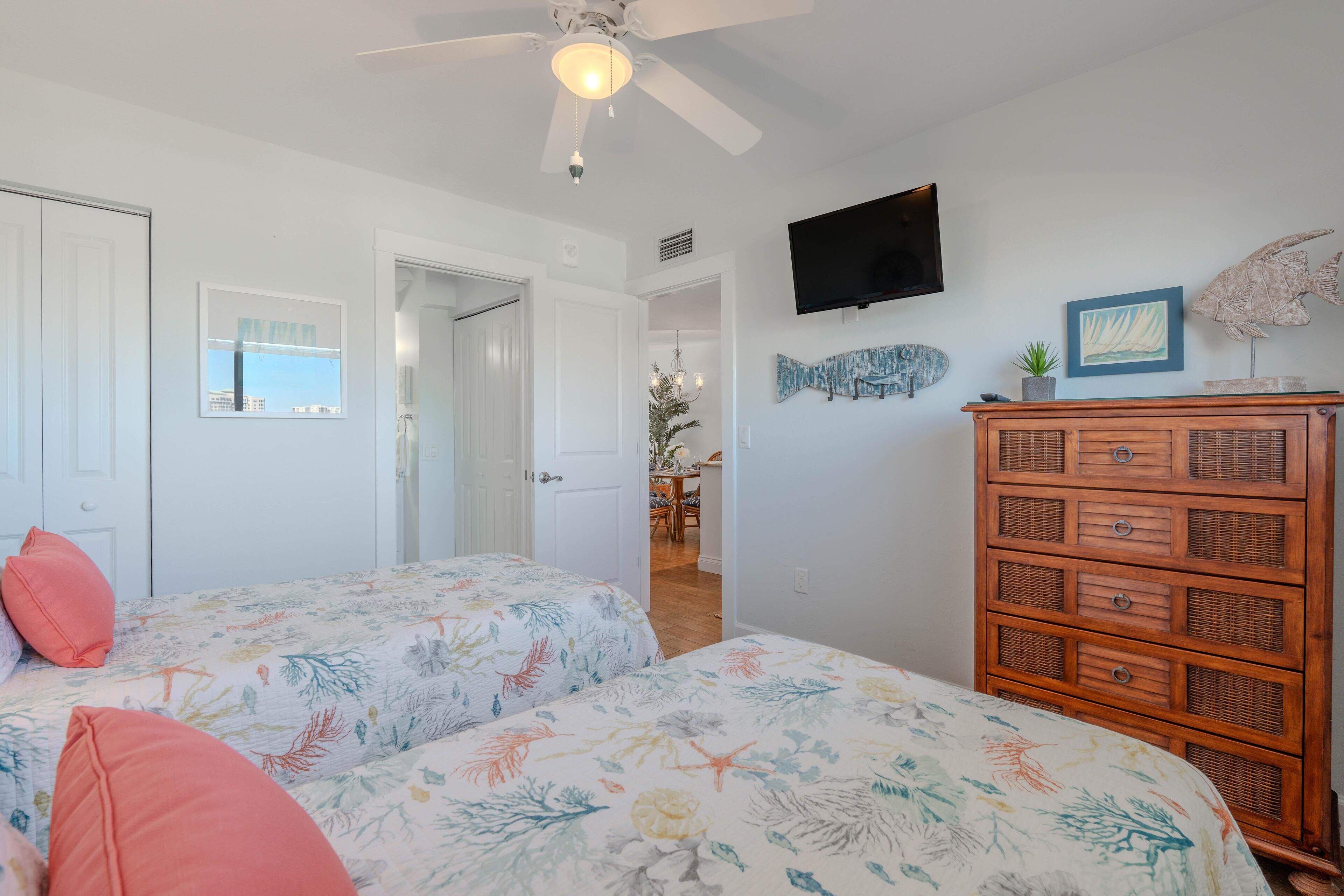 A bedroom with two beds, a ceiling fan, a TV, and a wooden dresser.